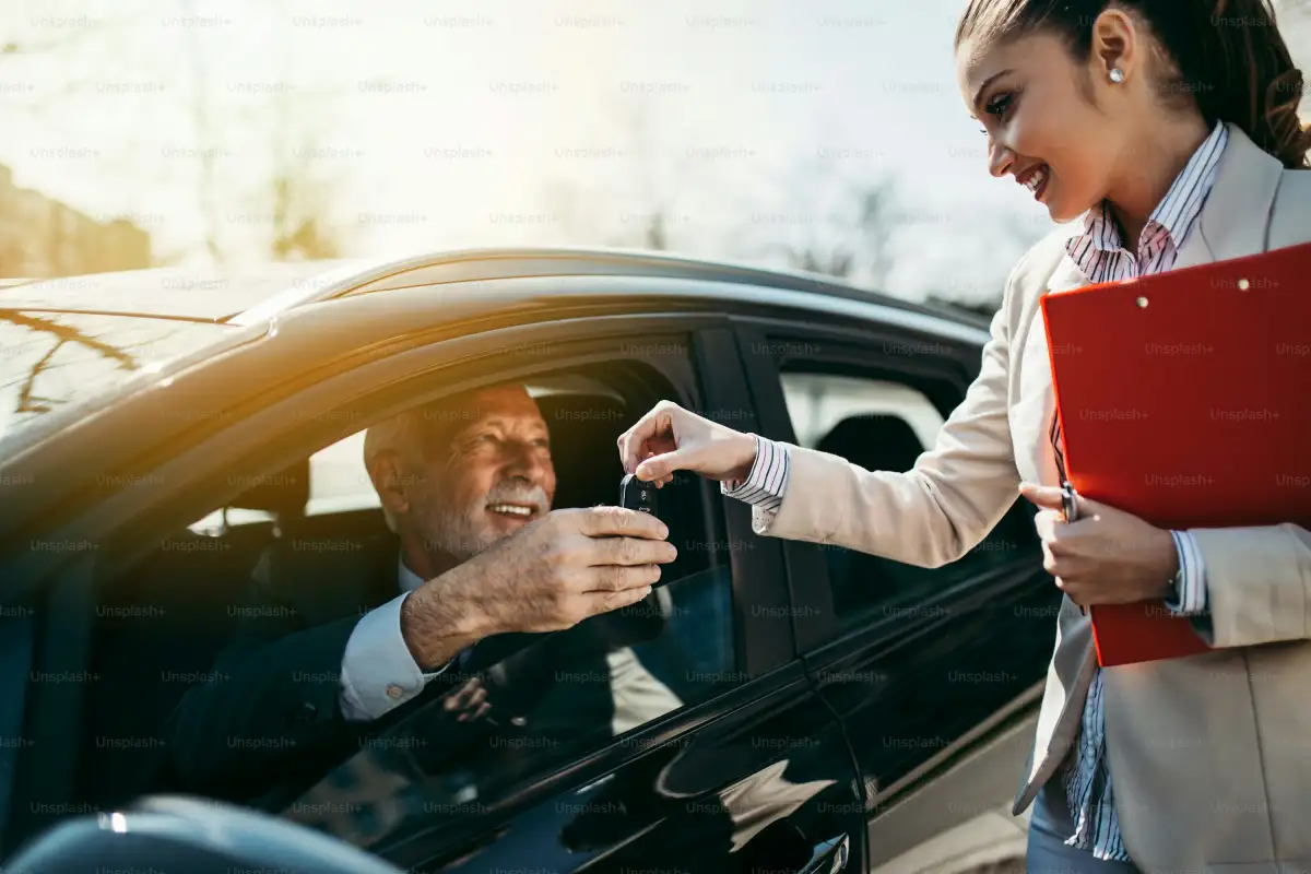 Beautiful young woman sales manager showing car specification to happy senior man buyer.